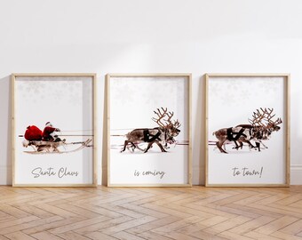 Pode incluir: Três quadros emoldurados que representam o Papai Noel e suas renas, pintados com aquarela. A primeira pintura mostra o Papai Noel em seu trenó com um saco de presentes. A segunda pintura mostra uma equipe de renas correndo. A terceira pintura mostra as renas correndo com o texto "to town!" abaixo. O texto sobre as renas na segunda pintura diz "is coming". O texto abaixo do Papai Noel na primeira pintura diz "Santa Claus".