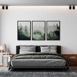 May include: A gray upholstered bed with a black frame and a gray blanket. Three framed black and white prints of a foggy forest scene hang above the bed.