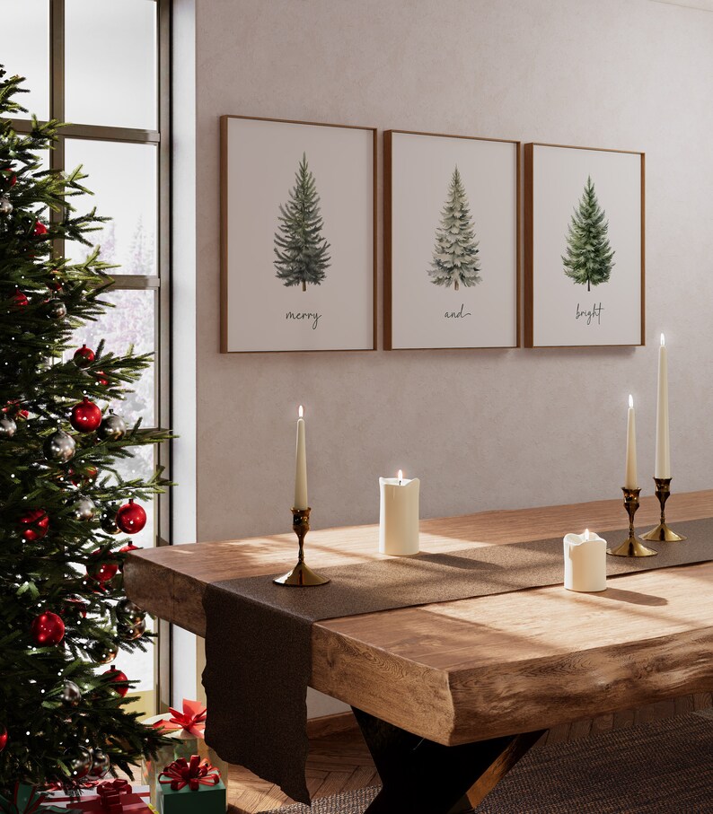 Pode incluir: Tr&ecirc;s pinturas de aquarela emolduradas de pinheiros com as palavras "merry", "and" e "bright" abaixo de cada &aacute;rvore. As pinturas est&atilde;o penduradas em uma parede branca sobre uma mesa de madeira com um corredor marrom e velas acesas.