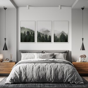 May include: A bedroom interior with a gray bed, two wooden nightstands, and three framed landscape photographs of a misty forest. The room has a modern minimalist design with white walls and black pendant lights.