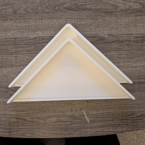 May include: Two white, triangular-shaped trays with raised edges. The trays are stacked slightly offset from one another, creating a layered appearance. Each tray features a smooth, matte surface and a clean, geometric design with sharp corners.