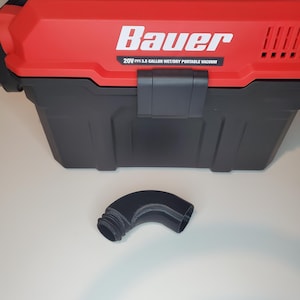 Puede incluir: Una aspiradora portátil húmeda/seca Bauer roja y negra de 20 V y 3,5 galones. La aspiradora tiene un mango negro y una boquilla de manguera negra.