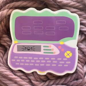 May include: Purple and green digital pet toy with a screen that says "Magic!" and a keyboard. The toy has a yellow button with a star on it.