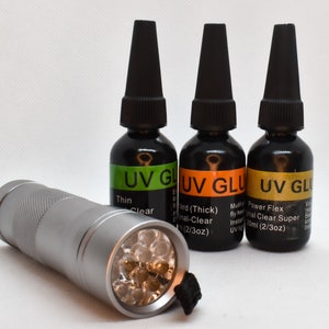 May include: Three bottles of UV glue in green, orange, and yellow packaging with labels that read "UV Glue". The bottles are labeled with different types of glue: Thin Clear, Hard (Thick) Normal-Clear, and Power Flex Normal Clear Super. A silver flashlight with a black strap is in the foreground.