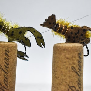 May include: Two green and brown fly fishing lures with yellow and gold accents, mounted on cork.