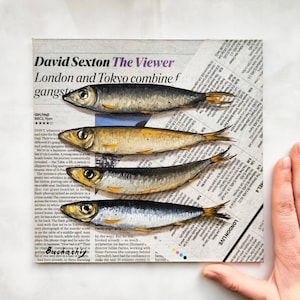 May include: Four small, silver, painted fish arranged in a row on a newspaper background. The fish are painted realistically with details like scales and fins. The newspaper text reads "David Sexton The Viewer London and Tokyo combine f gangste".