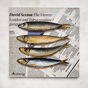 May include: A close-up of a newspaper clipping with the headline "David Sexton The Viewer" and the text "London and Tokyo combine f gangste" printed in black ink. Four silver fish are painted on the newspaper, with their tails extending off the edge of the page.