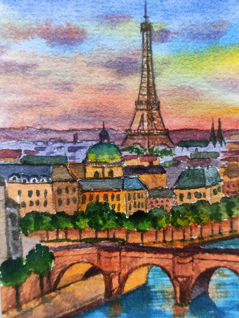 May include: Watercolor painting of the Eiffel Tower in Paris, France. The painting depicts the tower in the distance with a bridge and buildings in the foreground. The sky is a vibrant orange and pink sunset.