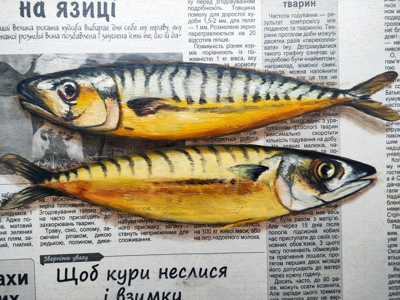 May include: Two yellow and silver mackerel fish painted on a newspaper background. The fish have dark stripes and are positioned horizontally. The newspaper has Ukrainian text.