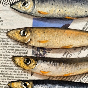 May include: A close-up of five painted fish, stacked on top of each other. The fish are painted in a realistic style, with details like scales, fins, and eyes. The fish are painted on a background of newspaper text, which is partially visible.