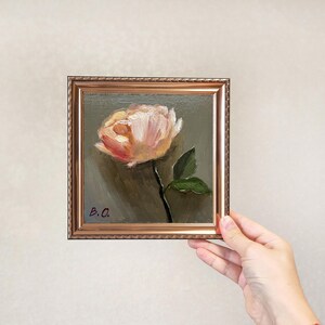 May include: A small framed painting of a single pink flower with green leaves on a dark green background. The painting is signed "B.O."