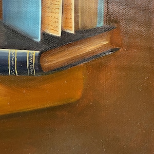 May include: A close-up of a stack of books with a blue book on top and a brown book on the bottom. The books are on a brown surface with the signature "Buchacha M." in gold lettering.