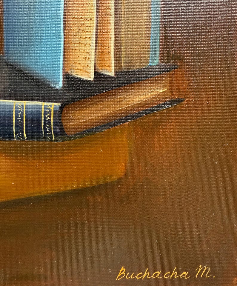 May include: A close-up of a stack of books with a blue book on top and a brown book on the bottom. The books are on a brown surface with the signature "Buchacha M." in gold lettering.