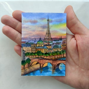 May include: Watercolor painting of the Eiffel Tower in Paris, France. The painting depicts the tower with a bridge in the foreground and a sunset sky in the background.