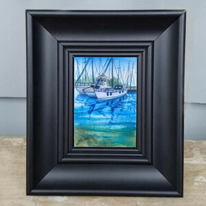 Puede incluir: Una pintura de acuarela enmarcada de dos veleros blancos atracados en un puerto deportivo. Los barcos est&aacute;n rodeados de agua azul con reflejos de los barcos y el cielo. La pintura est&aacute; enmarcada en un marco negro.