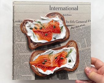 May include: Two slices of toasted bread topped with cream cheese and smoked salmon. The bread is on a newspaper with the headline "International" and the text "Its 6th General Election".