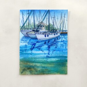 Puede incluir: Pintura acuarela de un puerto deportivo con varios veleros atracados. Los barcos son blancos con detalles azules y se reflejan en el agua azul. El agua es de color azul claro con ondas azules m&aacute;s oscuras. El cielo es de color azul claro.