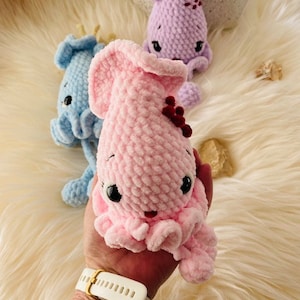 May include: Crochet octopus plush toys in pink, blue, and purple. The toys have large black eyes and small red accents. These soft, fluffy toys are ideal for children or as decorative items.