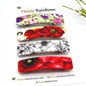 May include: Four rectangular hair clips attached to a white display card labeled Honey Rainbows. The clips feature floral patterns including purple and pink flowers, red poppies, black and white line art flowers, and a vibrant red poppy design.