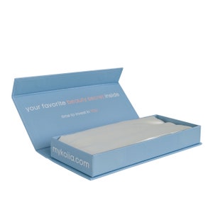 May include: A light blue box with the text "your favorite beauty secret inside time to invest in you" and the website "mykoila.com" printed on the front. The box is open and the inside is lined with white satin.
