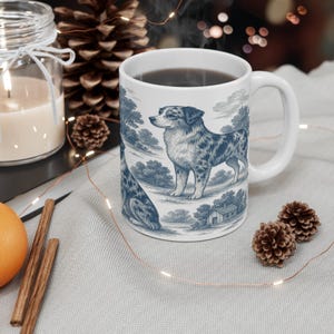 May include: White ceramic mug featuring a blue and white illustration of a dog in a pastoral scene. The mug is filled with a dark liquid and has a curved handle. The design resembles a classic toile pattern.