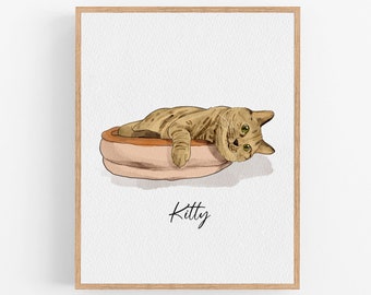 Puede incluir: Una impresión en acuarela enmarcada de un gato acostado en una cama. El gato tiene rayas marrones y beige, ojos verdes y descansa sobre una cama rosa y marrón. La palabra "Kitty" está escrita en cursiva debajo.