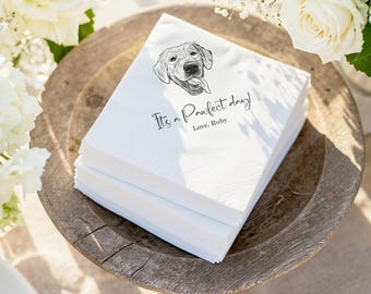 Puede incluir: Una pila de servilletas de papel blancas con una ilustración en blanco y negro de un perro. El texto "It's a Pawfect day! Love, Ruby" está impreso. Las servilletas están en un cuenco de madera, rodeadas de flores blancas.