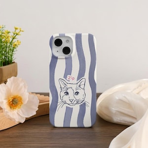 May include: A phone case with a white and blue striped pattern. The case features a black and white illustration of a cat's face with the word "zip" above it. The case is on a wooden surface.