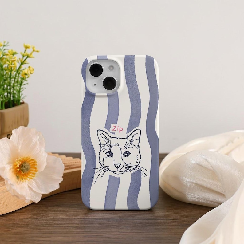 May include: A phone case with a white and blue striped pattern. The case features a black and white illustration of a cat's face with the word "zip" above it. The case is on a wooden surface.