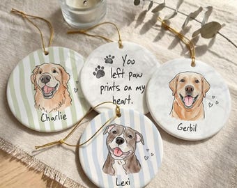 May include: Four round ceramic ornaments with gold hanging strings. Three feature illustrated dog portraits with names Charlie, Gerbil, and Lexi. One ornament displays the text You left paw prints on my heart with black paw print icons.