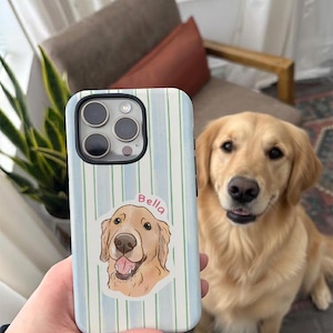May include: A light blue and white striped phone case featuring a golden retriever illustration with the name "Bella". The case is held in front of a golden retriever dog.