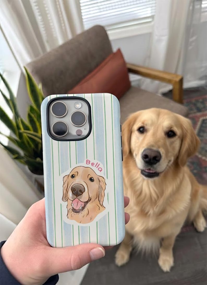 May include: A light blue and white striped phone case featuring a golden retriever illustration with the name "Bella". The case is held in front of a golden retriever dog.