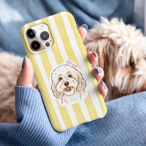 May include: Yellow and white striped phone case featuring a cartoon illustration of a dog with the name "Olive" above it. The case is held in a person's hand.