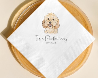 Puede incluir: Servilleta cuadrada blanca con una ilustración de un perro marrón claro. El texto "It's a Pawfect day!" está escrito debajo, con espacio para un nombre. La servilleta está sobre un plato de madera.