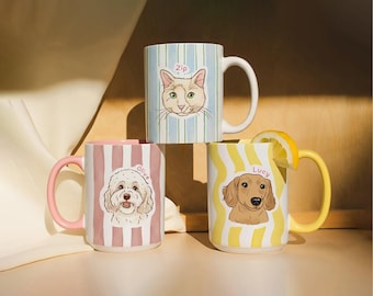 Puede incluir: Tres tazas de cerámica con ilustraciones de animales. Una taza tiene una cara de gato y el nombre "Zip" sobre un fondo a rayas azules y blancas. Otra taza tiene una cara de perro y el nombre "Olive" sobre un fondo a rayas rosas y blancas. La tercera taza tiene una cara de perro y el nombre "Lucy" sobre un fondo ondulado amarillo y blanco.
