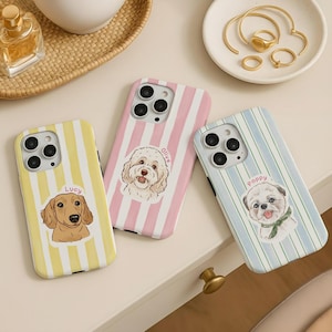 May include: Three phone cases with dog illustrations. One case is yellow with vertical stripes and a dachshund illustration with the name "Lucy". Another is pink with vertical stripes and a dog illustration with the name "Olive". The third is blue with vertical stripes and a dog illustration with the name "Poppy".