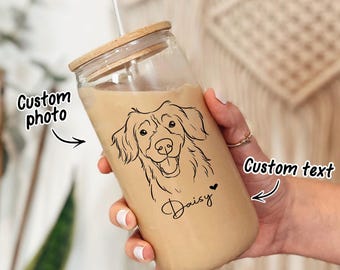 Puede incluir: Un vaso de vidrio transparente con tapa de madera, lleno de una bebida marrón claro. El vaso presenta un dibujo lineal negro de la cara de un perro y el nombre "Daisy". También se ven las palabras "Custom photo" y "Custom text".