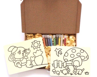May include: A brown cardboard box with a lid open, revealing two white cards with black line drawings of a rabbit and a mushroom. The box also contains a set of ten small tubes of colorful sand art.