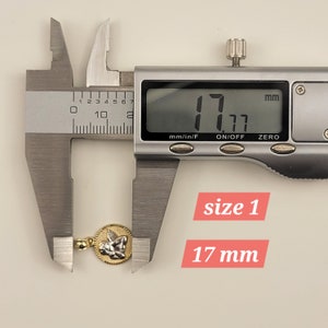 May include: A silver caliper measuring a gold angel pendant. The caliper reads 17 mm. The text "size 1" and "17 mm" are written below the caliper.
