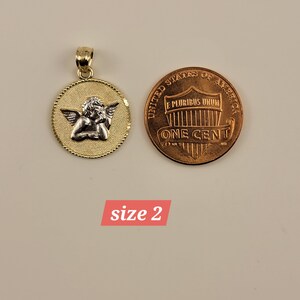 May include: Gold and silver angel pendant charm with a halo, wings, and a sleeping cherub. The pendant is shown next to a US penny for size comparison. "size 2" is written below the image.