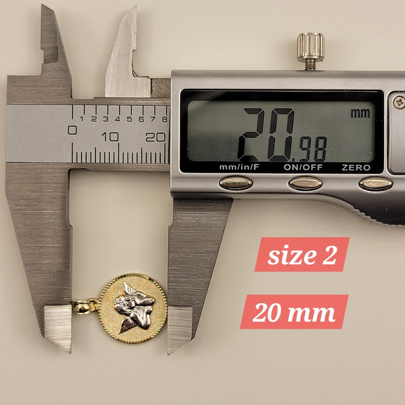 May include: A gold-toned pendant with a detailed angel design, measured at 20 mm in diameter using a digital caliper.