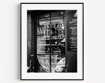 Puede incluir: Una foto en blanco y negro de una fachada de restaurante parisino con el texto "RESTAURANT AU PETIT CREUX" y "Service non stop" escrito en la ventana. El letrero también dice "Soupe à l'oignon".