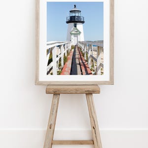 Vertical photograph of Brant Point Lighthouse in Nantucket, viewed straight down the weathered boardwalk with a bright blue sky and soft coastal light.