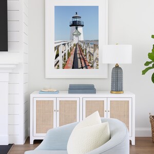 Vertical photograph of Brant Point Lighthouse in Nantucket, viewed straight down the weathered boardwalk with a bright blue sky and soft coastal light.