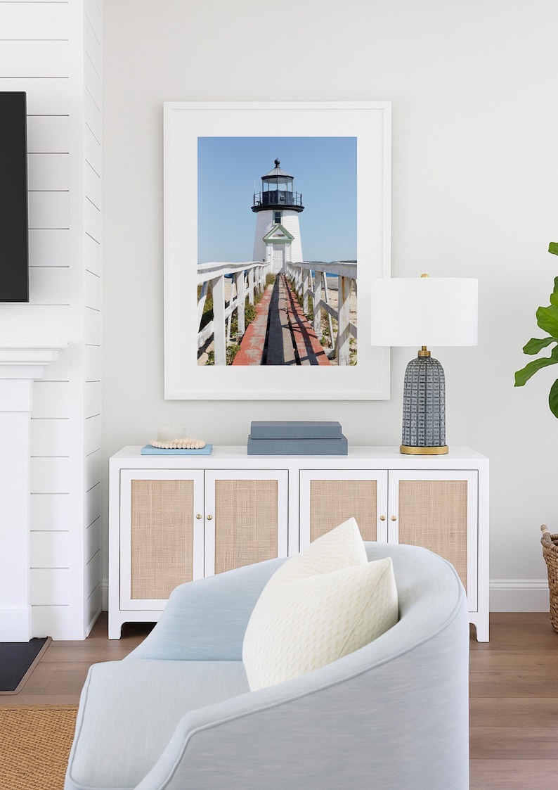 Vertical photograph of Brant Point Lighthouse in Nantucket, viewed straight down the weathered boardwalk with a bright blue sky and soft coastal light.