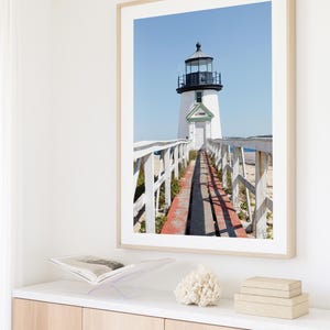 Vertical photograph of Brant Point Lighthouse in Nantucket, viewed straight down the weathered boardwalk with a bright blue sky and soft coastal light.