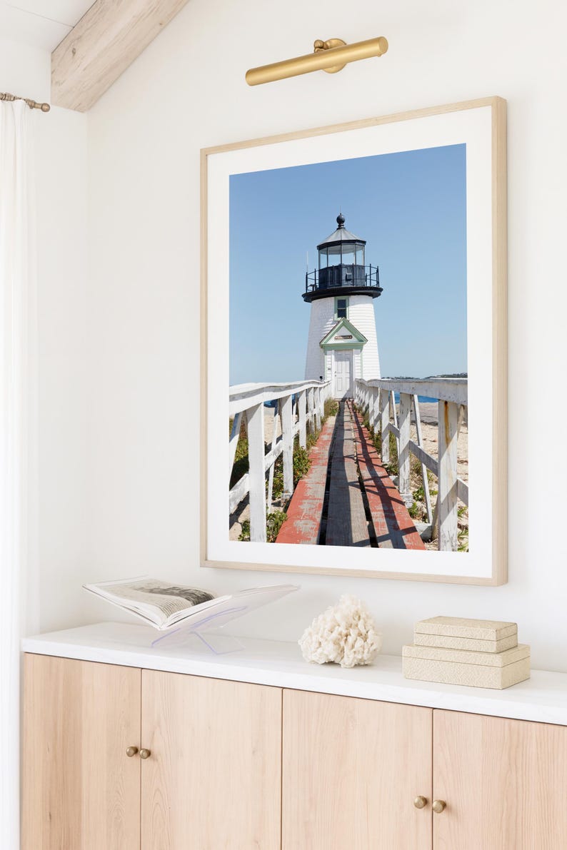 Vertical photograph of Brant Point Lighthouse in Nantucket, viewed straight down the weathered boardwalk with a bright blue sky and soft coastal light.