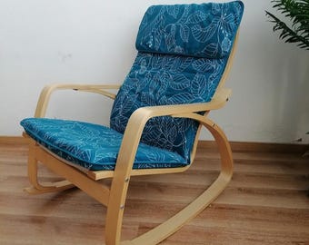 May include: A wooden rocking chair with a teal blue cushion featuring a white leaf pattern. The chair has a curved back and a wide seat.
