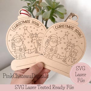 May include: Two round wooden Christmas ornaments featuring laser-engraved designs of Santa Claus, a reindeer, a snowman, and a Christmas tree. Each ornament is inscribed with the text CHRISTMAS 2026 and includes a blank space for personalization.