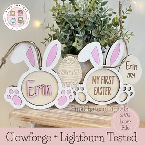Puede incluir: Un adorno de conejo de Pascua de madera con orejas rosas y huellas de patas. El adorno tiene un círculo en el centro con el nombre "Erin" y el texto "Mi primera Pascua". También hay un círculo más pequeño con el nombre "Erin" y el año "2024".